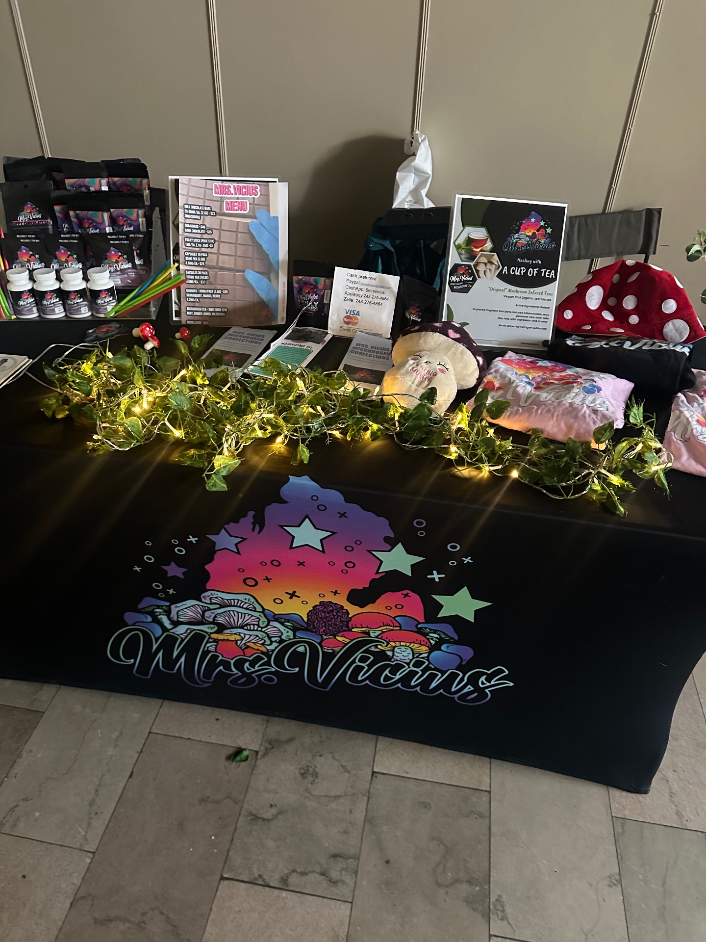 Mrs. Vicius community market booth with mushroom teas, educational materials, and colorful artwork